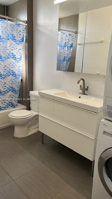 full bathroom featuring toilet, vanity, shower / tub combo with curtain, and stacked washer / dryer