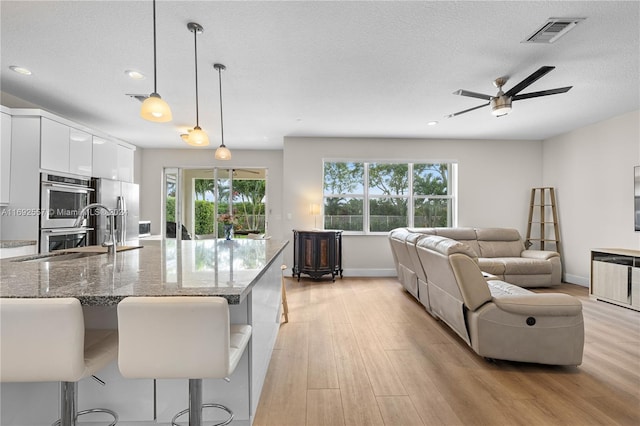 kitchen with stone counters, hanging light fixtures, a kitchen breakfast bar, white cabinets, and light wood-type flooring