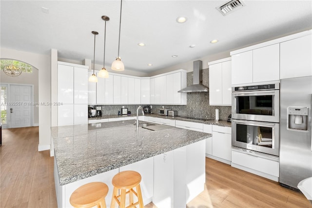 kitchen with white cabinetry, light hardwood / wood-style flooring, and wall chimney range hood