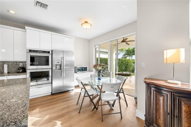 kitchen featuring backsplash, white cabinets, dark stone countertops, light wood-type flooring, and appliances with stainless steel finishes