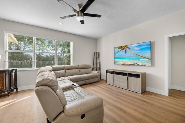 living room with ceiling fan, light wood-type flooring, and a textured ceiling