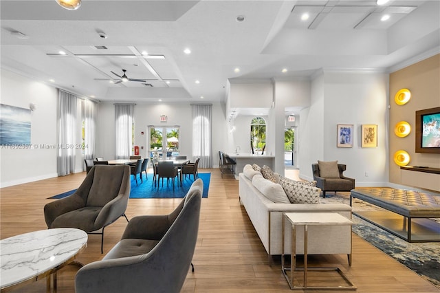 living room featuring ceiling fan, light hardwood / wood-style floors, coffered ceiling, and ornamental molding