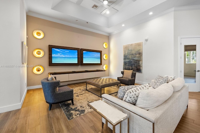 living room with a raised ceiling, crown molding, and light hardwood / wood-style flooring