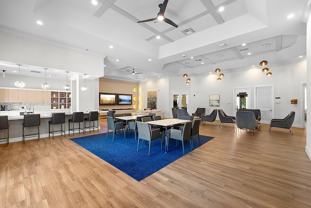 dining space with ceiling fan, coffered ceiling, a raised ceiling, crown molding, and light wood-type flooring