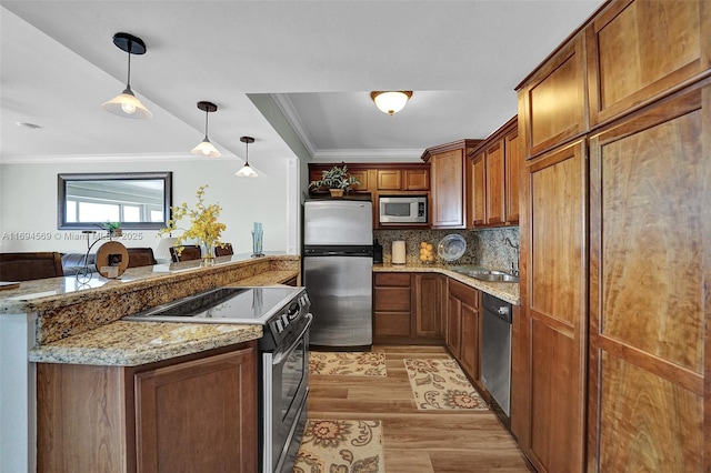 kitchen featuring stainless steel appliances, ornamental molding, a sink, light wood-type flooring, and a peninsula