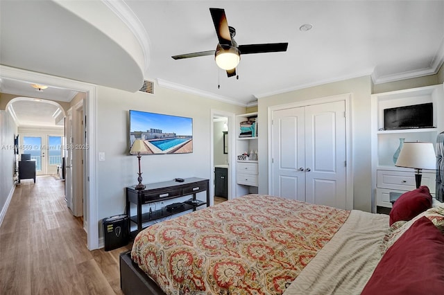 bedroom featuring arched walkways, a closet, visible vents, ornamental molding, and wood finished floors