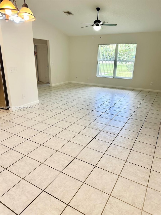 empty room featuring vaulted ceiling, light tile patterned flooring, and ceiling fan with notable chandelier