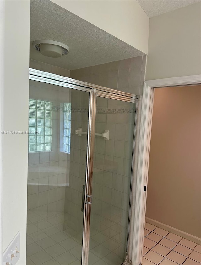 bathroom with tile patterned flooring, a textured ceiling, and a shower with shower door