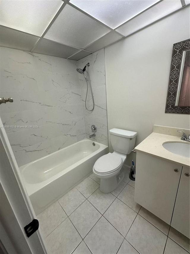 full bathroom with tile patterned floors, a drop ceiling, vanity, tiled shower / bath combo, and toilet