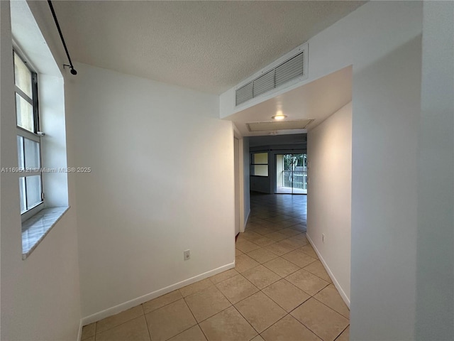 hallway featuring light tile patterned floors, visible vents, baseboards, and a textured ceiling