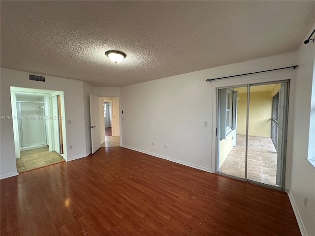 spare room with visible vents, a textured ceiling, baseboards, and wood finished floors