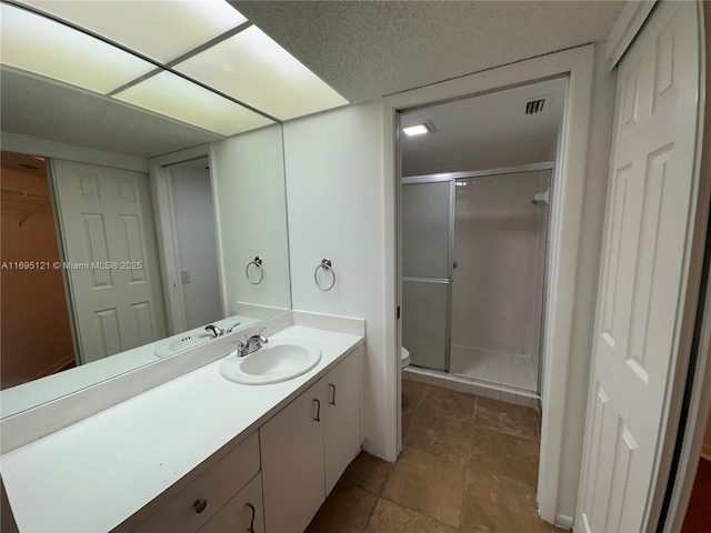 full bathroom featuring visible vents, toilet, a textured ceiling, a shower stall, and vanity