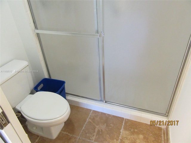 bathroom featuring tile patterned flooring, a shower with shower door, and toilet