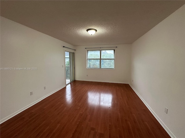 empty room with a textured ceiling, dark wood-type flooring, and baseboards