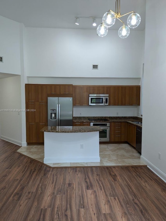 kitchen featuring dark stone counters, stainless steel appliances, sink, wood-type flooring, and decorative light fixtures