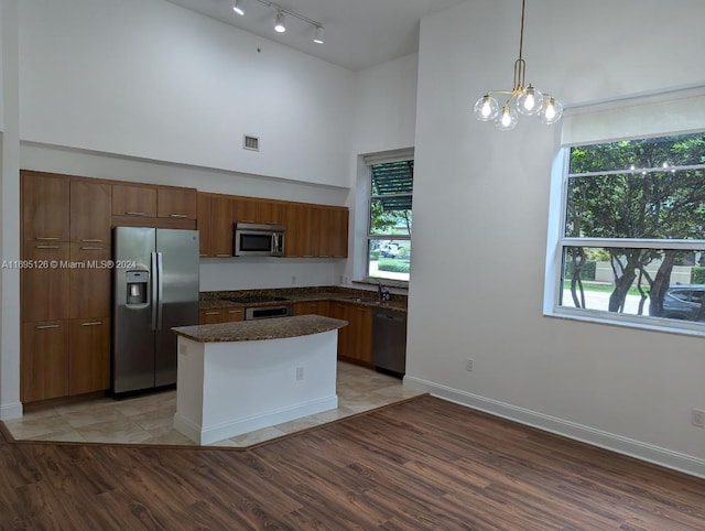 kitchen with light wood-type flooring, stainless steel appliances, a towering ceiling, and a chandelier