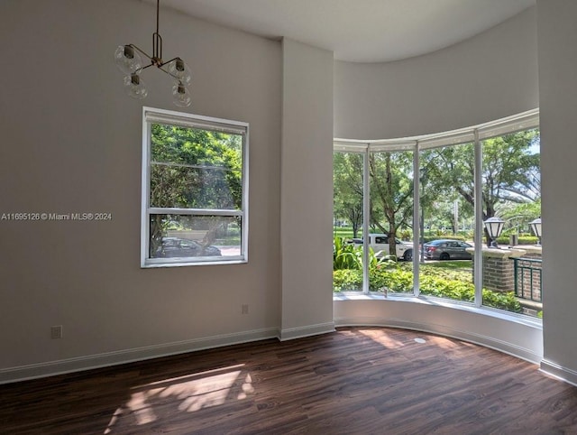 empty room with dark wood-type flooring, a high ceiling, and an inviting chandelier