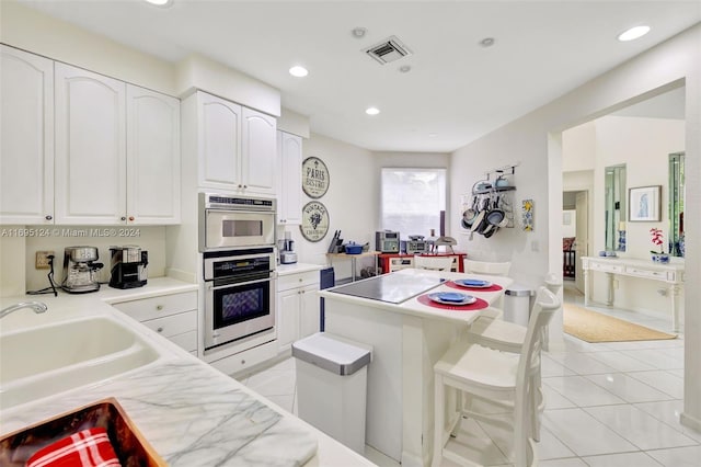 kitchen with white cabinets, light tile patterned floors, a kitchen island, and sink