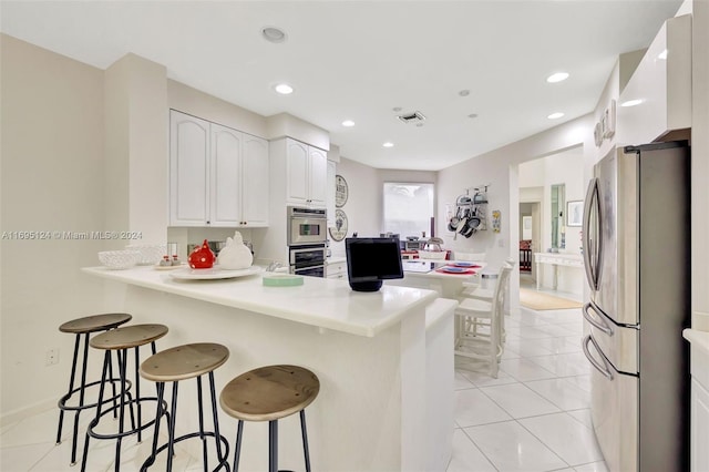 kitchen with white cabinets, appliances with stainless steel finishes, light tile patterned flooring, kitchen peninsula, and a breakfast bar area