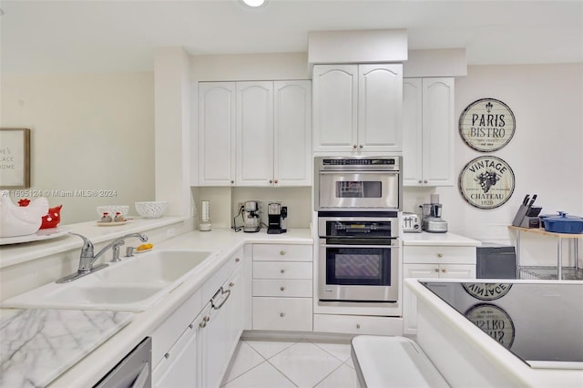 kitchen featuring dishwashing machine, double oven, sink, white cabinets, and light tile patterned flooring