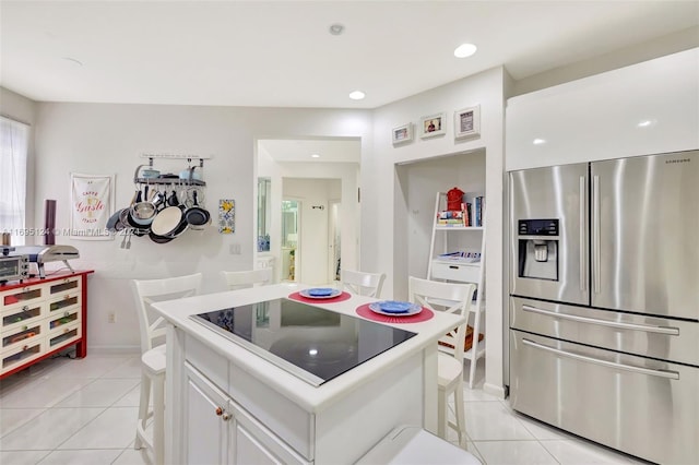 kitchen with a kitchen bar, stainless steel fridge, black electric stovetop, a kitchen island, and white cabinetry