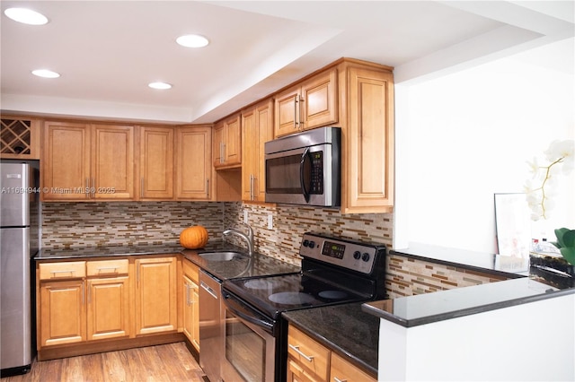 kitchen with tasteful backsplash, sink, dark stone counters, light hardwood / wood-style floors, and stainless steel appliances