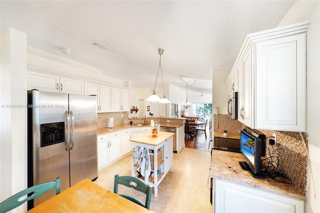 kitchen with hanging light fixtures, stainless steel appliances, kitchen peninsula, decorative backsplash, and white cabinets