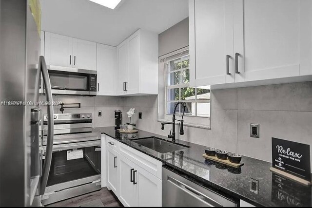 kitchen with appliances with stainless steel finishes, white cabinetry, dark stone countertops, and sink