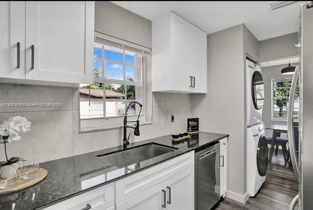 kitchen with a healthy amount of sunlight, white cabinetry, stainless steel dishwasher, and stacked washer / drying machine