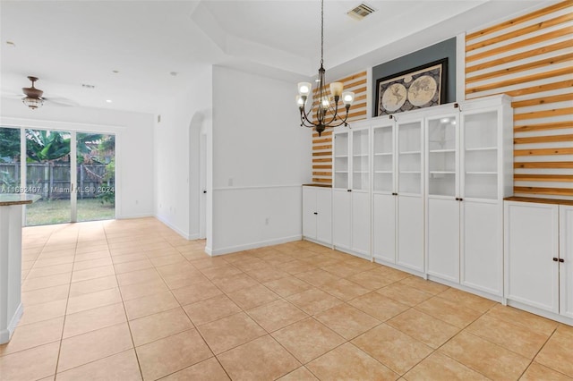 tiled empty room featuring ceiling fan with notable chandelier and a raised ceiling