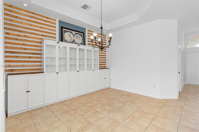 unfurnished dining area with a chandelier, light tile patterned floors, and a tray ceiling