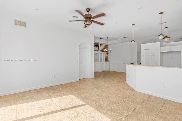 unfurnished living room with ceiling fan, light tile patterned flooring, and a tray ceiling