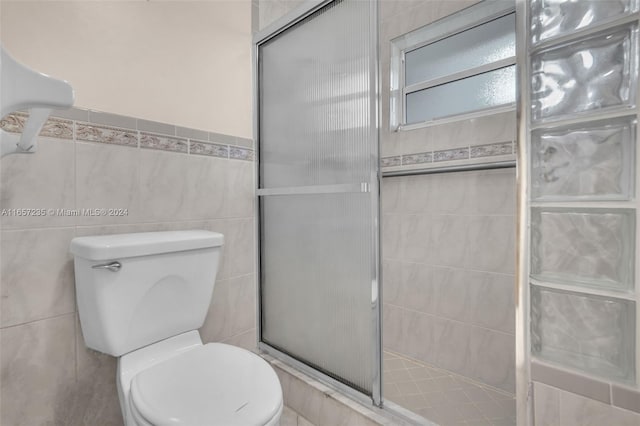 bathroom with an enclosed shower, toilet, and tile walls