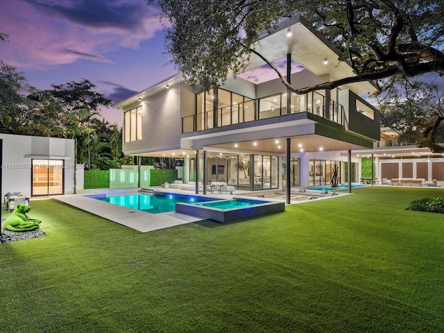 back house at dusk featuring a lawn, a balcony, and a patio