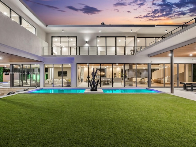 back house at dusk featuring a patio area and a lawn