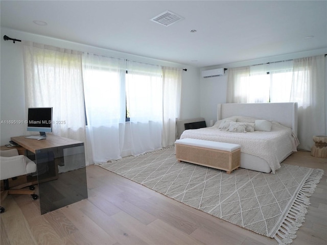 bedroom with a wall mounted air conditioner and light hardwood / wood-style floors