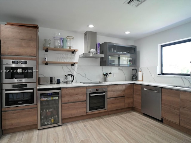 kitchen with appliances with stainless steel finishes, light wood-type flooring, backsplash, beverage cooler, and wall chimney range hood