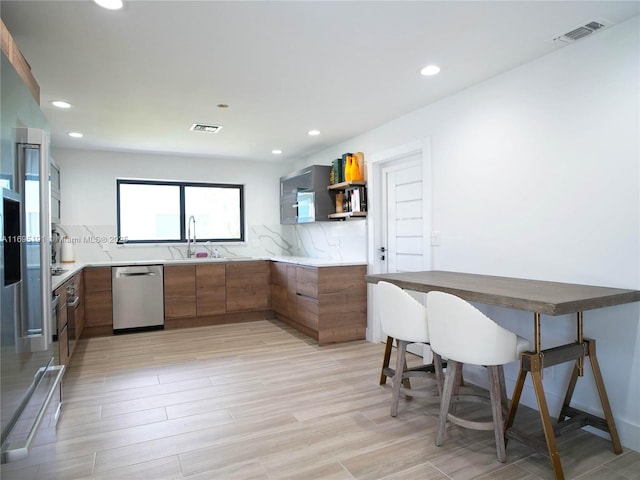 kitchen featuring decorative backsplash, light hardwood / wood-style floors, stainless steel dishwasher, and sink