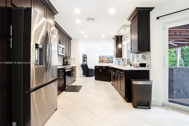 kitchen with appliances with stainless steel finishes, a textured ceiling, tasteful backsplash, and hanging light fixtures