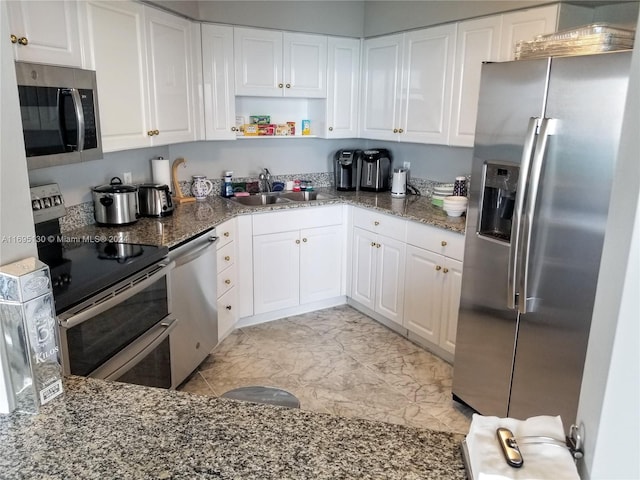 kitchen with stainless steel appliances, white cabinetry, dark stone counters, and sink