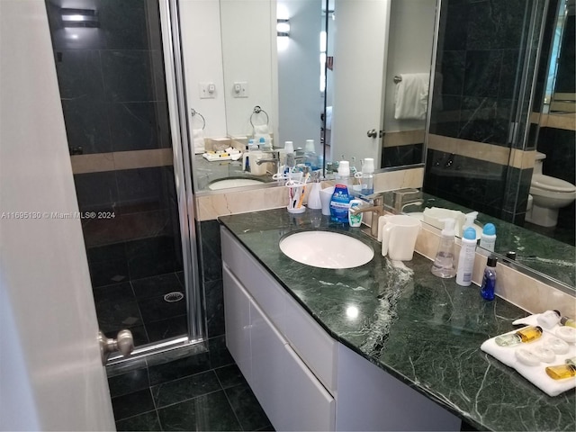 bathroom featuring tile patterned floors, vanity, toilet, and a shower with door