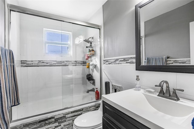 full bathroom with vanity, toilet, tile walls, and bath / shower combo with glass door