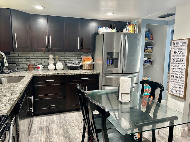 kitchen featuring backsplash, sink, light stone countertops, dark brown cabinets, and stainless steel fridge with ice dispenser