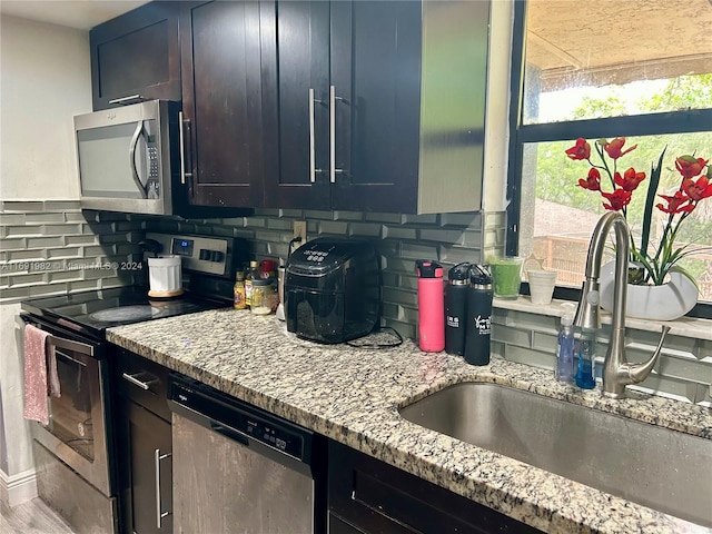 kitchen with decorative backsplash, stainless steel appliances, light stone counters, and sink