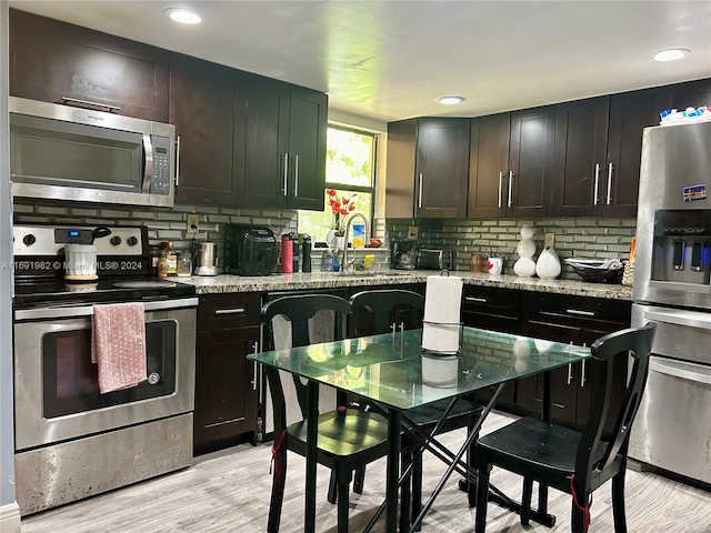 kitchen with appliances with stainless steel finishes, light wood-type flooring, tasteful backsplash, light stone counters, and sink