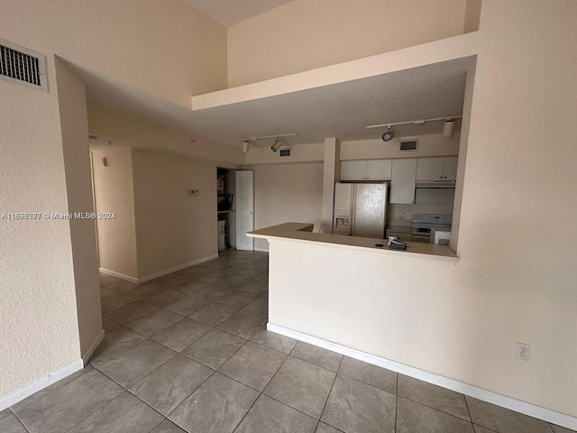 kitchen with white appliances, rail lighting, kitchen peninsula, light tile patterned floors, and white cabinetry