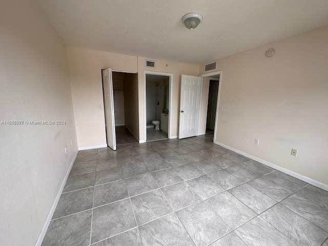 unfurnished bedroom featuring tile patterned floors, connected bathroom, and a closet