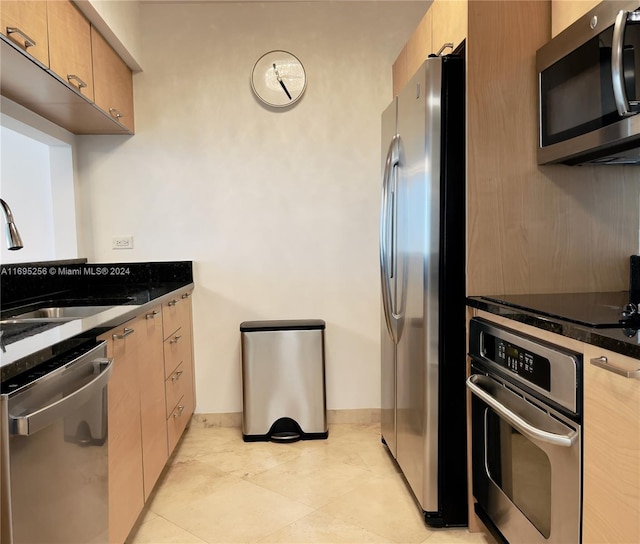 kitchen with appliances with stainless steel finishes, dark stone counters, sink, light brown cabinets, and light tile patterned floors