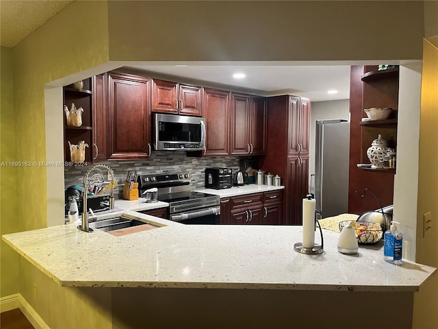 kitchen featuring light stone countertops, sink, stainless steel appliances, backsplash, and kitchen peninsula