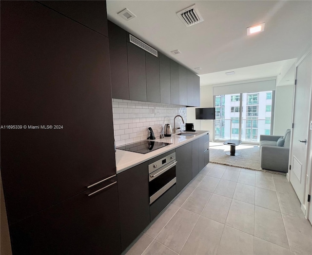 kitchen featuring tasteful backsplash, stainless steel oven, black electric cooktop, sink, and light tile patterned floors